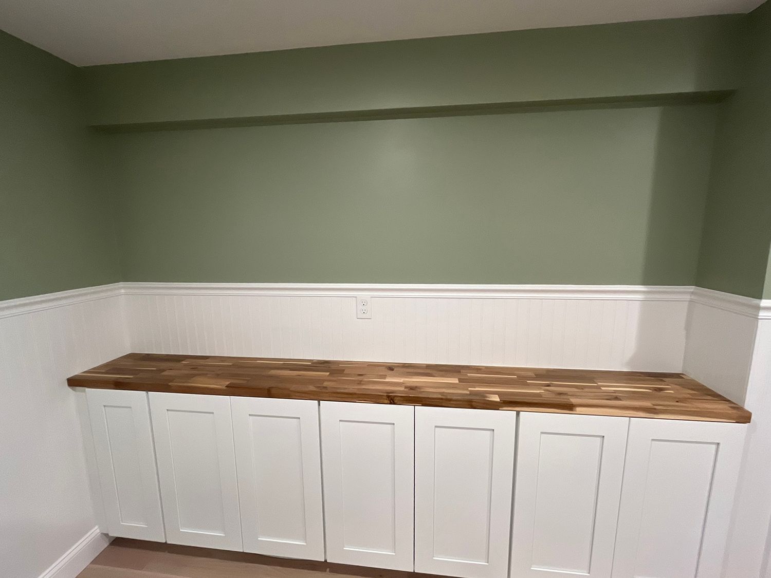 Built-in white cabinets with a wood countertop against a green wall with white wainscoting.