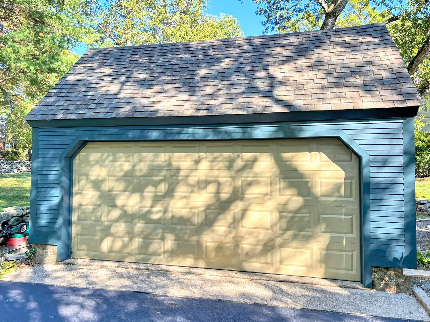 Tan garage door on blue-green building with grey roof.