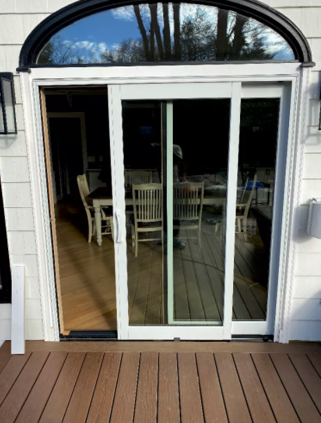 Sliding glass door, one panel open, framed with arched transom window, on wooden deck.