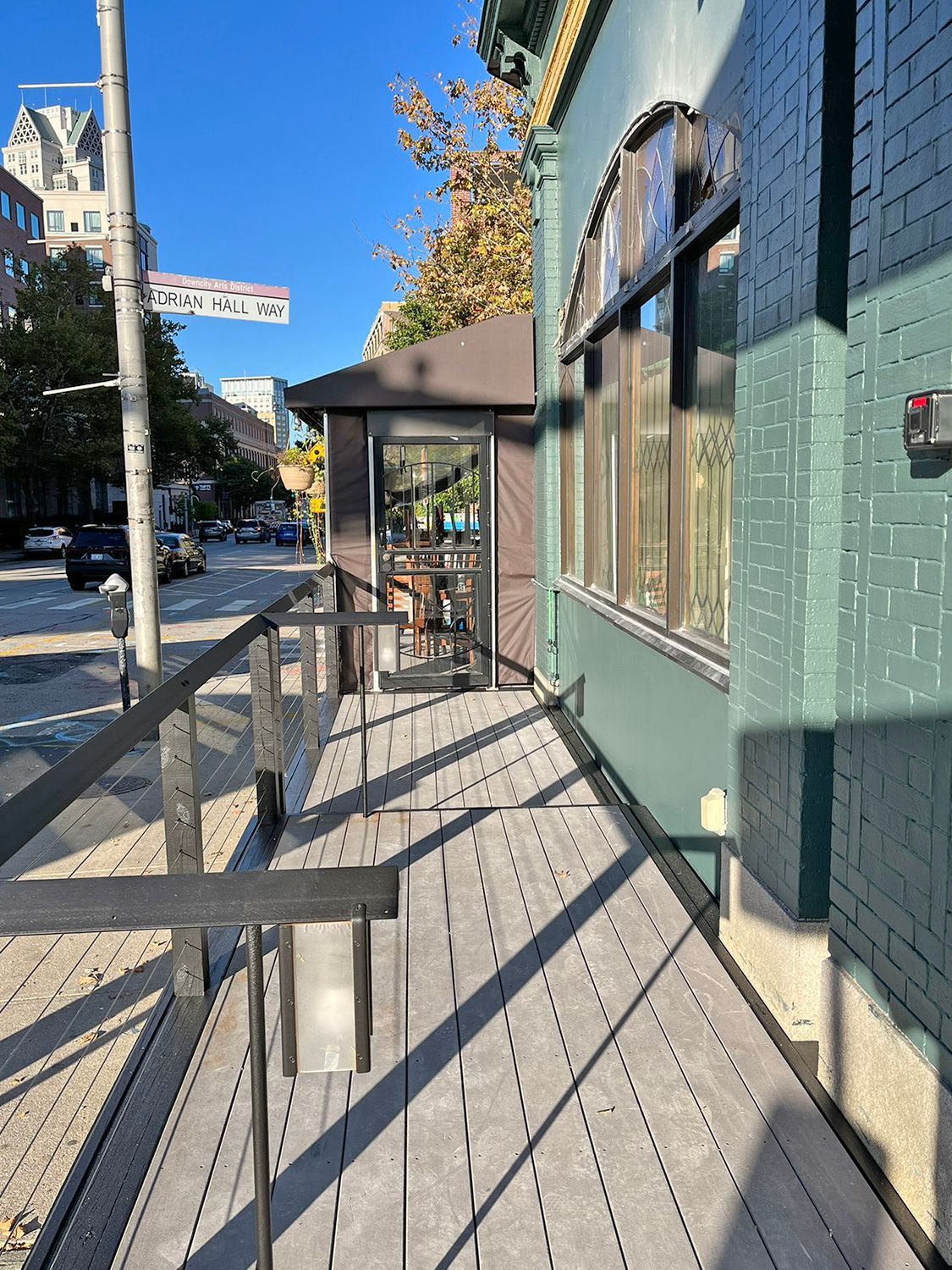Wooden deck and building exterior along a city street. Brown door, green building, and street sign visible.