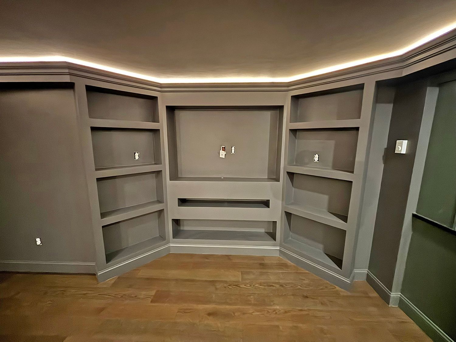 Built-in bookshelves and TV space in a room with wood floors and recessed lighting. Dark gray paint.