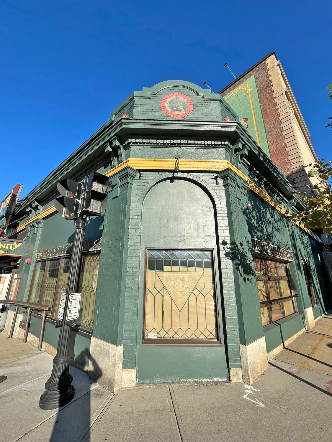 Green building on a street corner with arched windows and a decorative circular emblem.