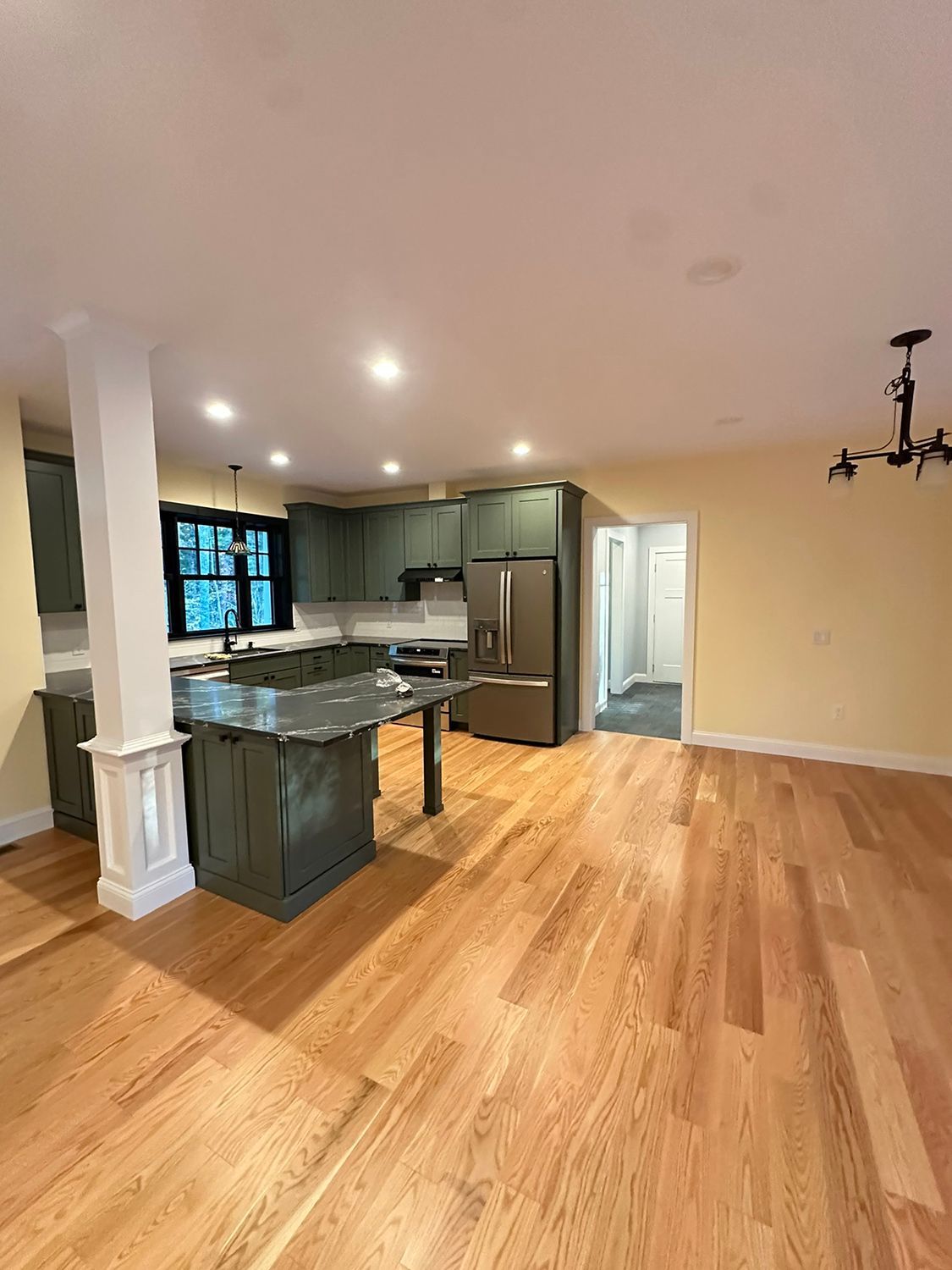Kitchen with sage green cabinets, an island, stainless steel refrigerator, and wood flooring.