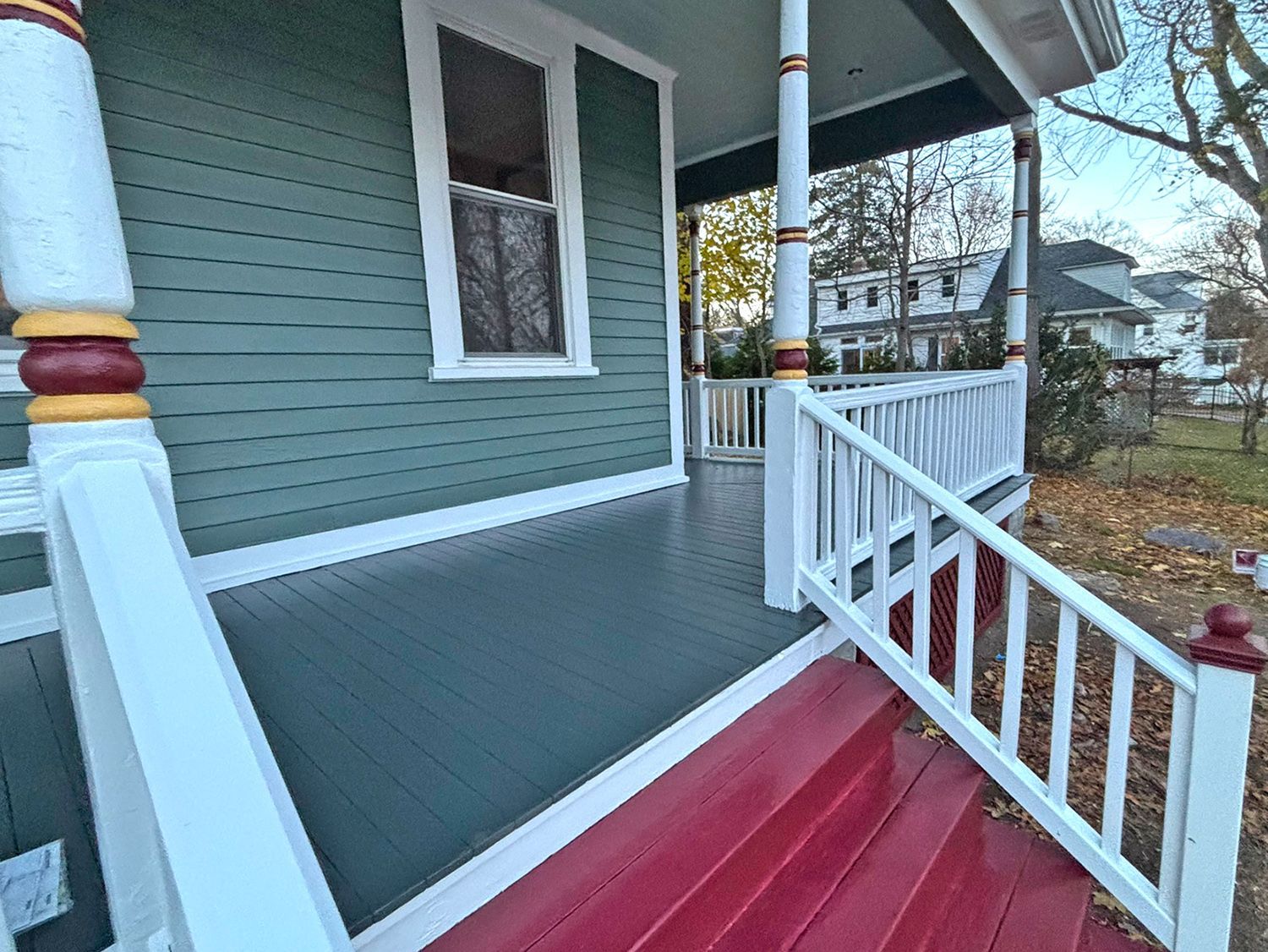 Green house porch with white railing, red steps, and ornate pillar details.