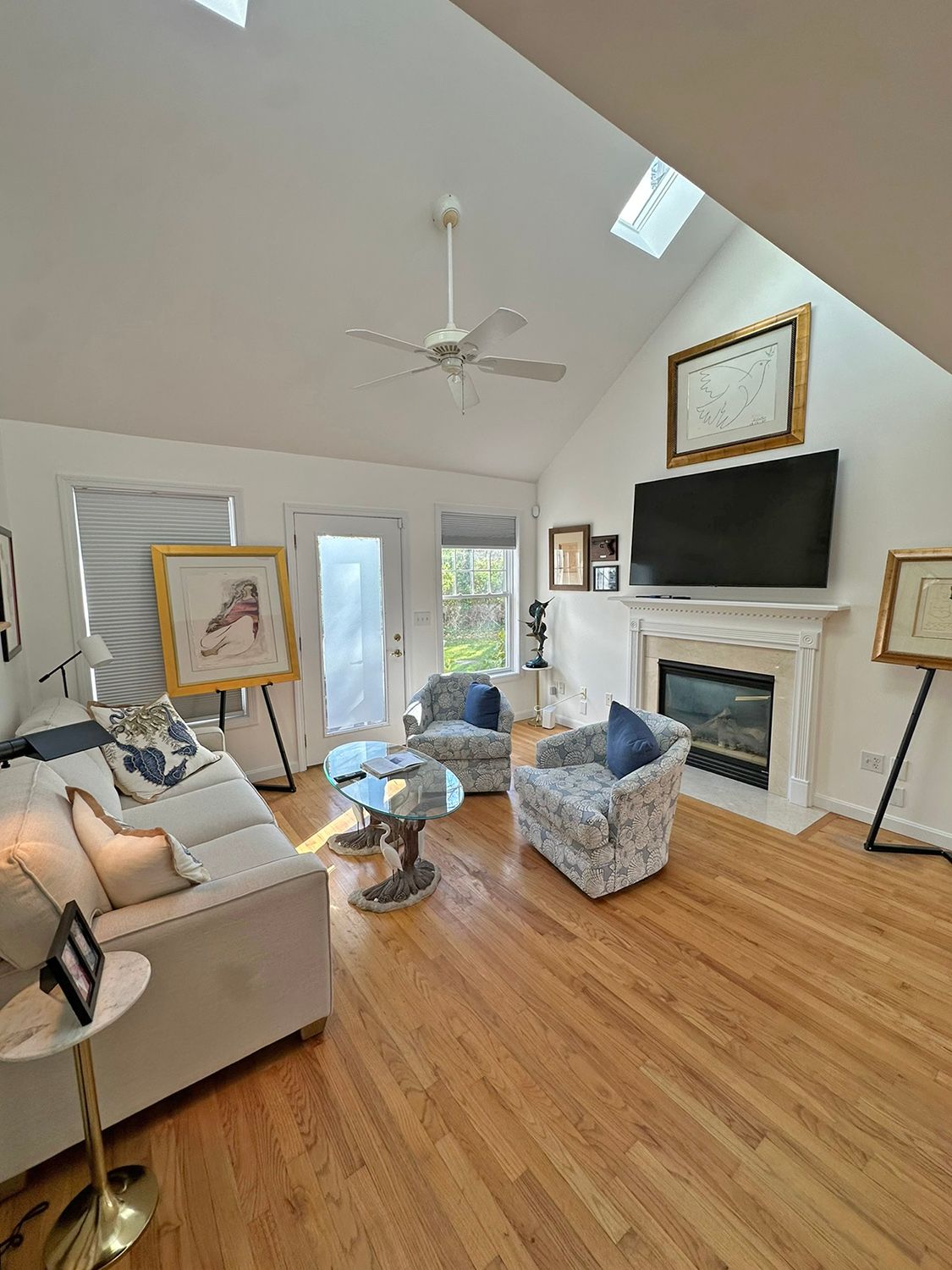 Bright living room with white walls, skylights, fireplace, hardwood floors, and art.