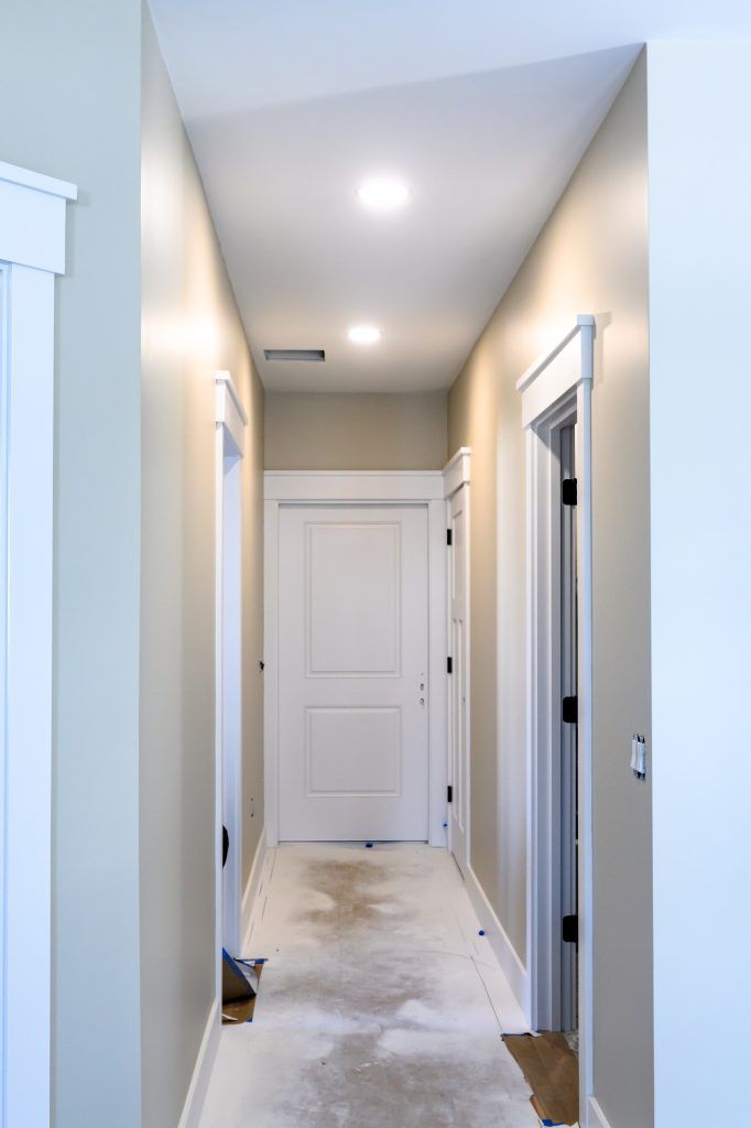 Narrow hallway with white doors, trim, and pale walls; overhead lights.