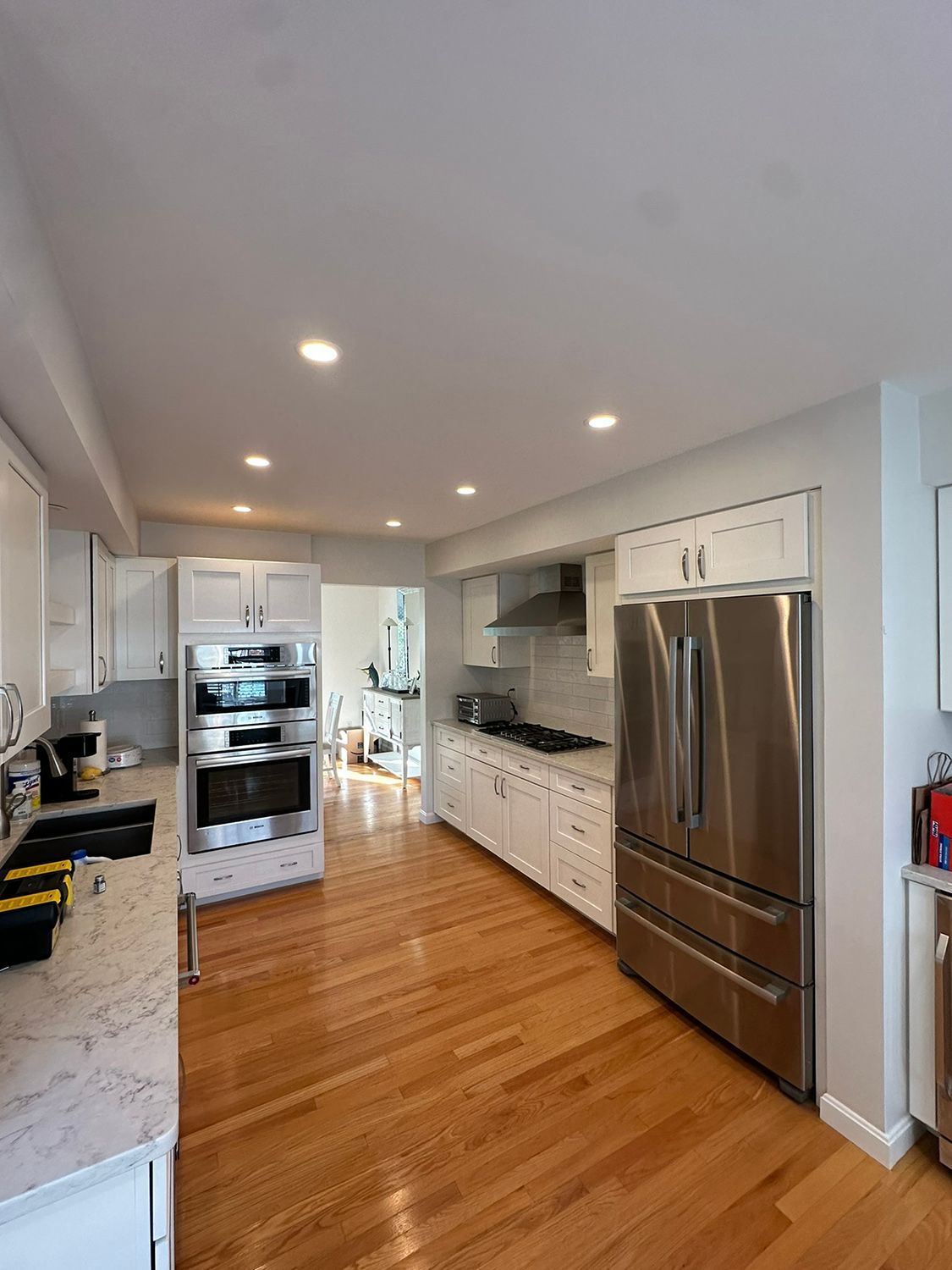 Bright white kitchen with stainless steel appliances, light wood floors, and recessed lighting.