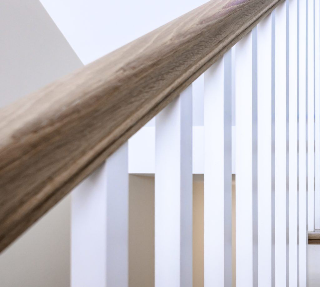 Wooden handrail over white vertical spindles on staircase.