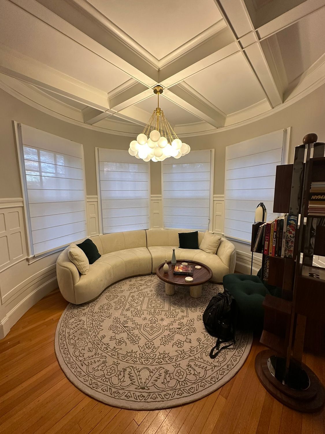 Curved ivory sofa in a bay window room with a patterned rug and chandelier.