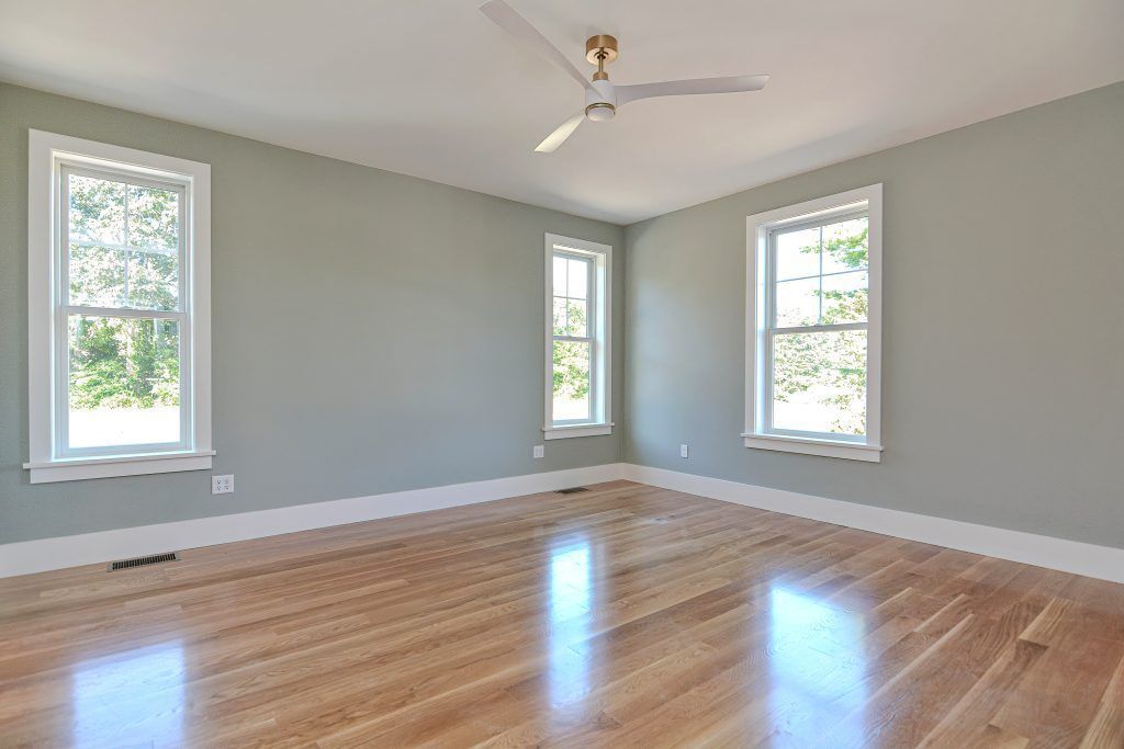 Empty room with wood floor, pale green walls, three windows with white trim, and a ceiling fan.