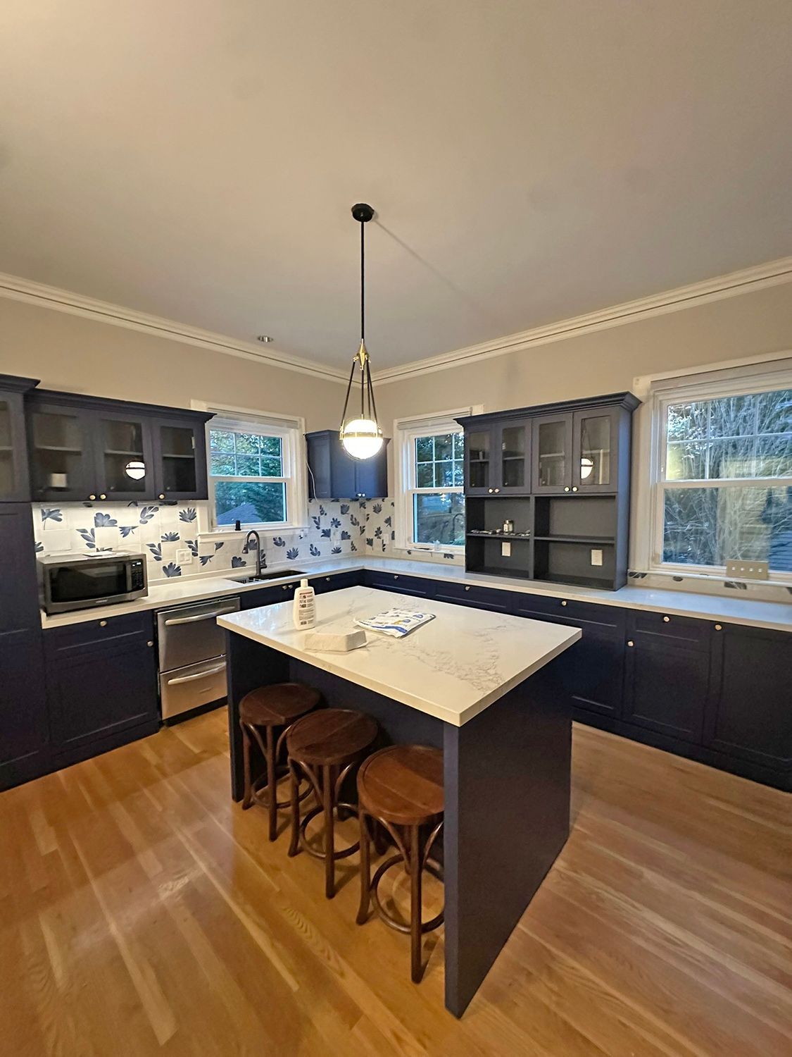 Kitchen with navy cabinets, marble countertops, wooden floors, and a central island with bar stools.
