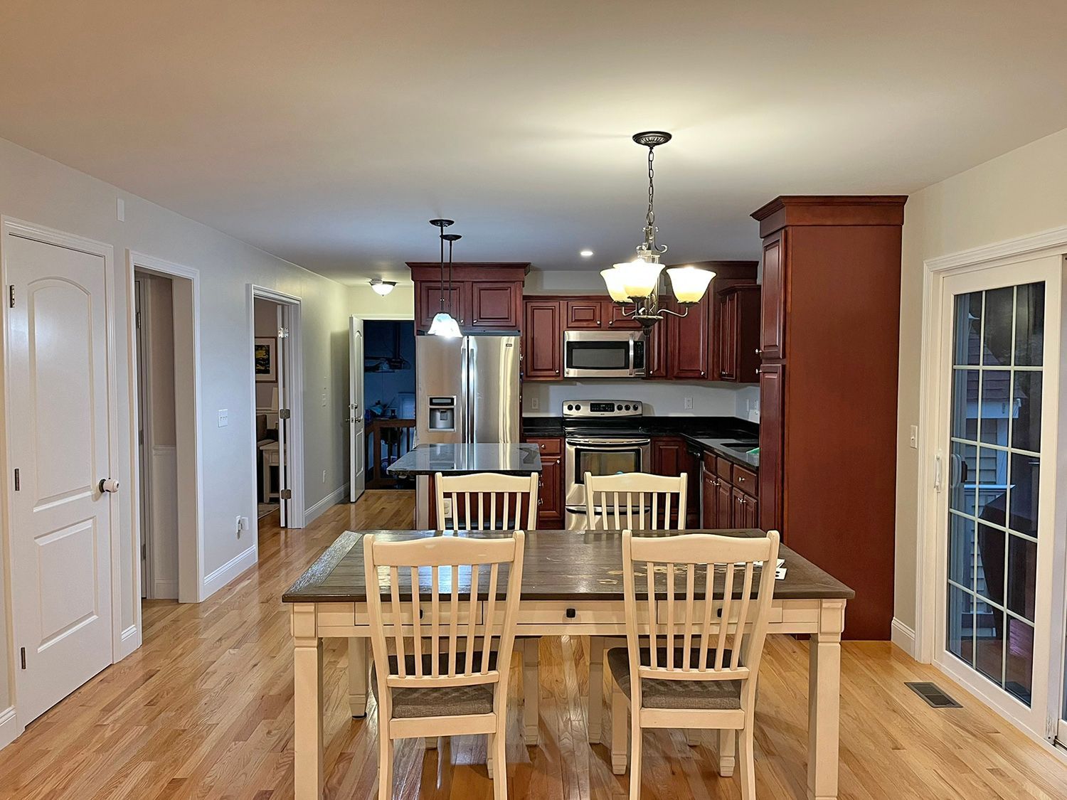 Kitchen with wooden floors, dining table, and dark red cabinets. Sliding glass door and white doors visible.