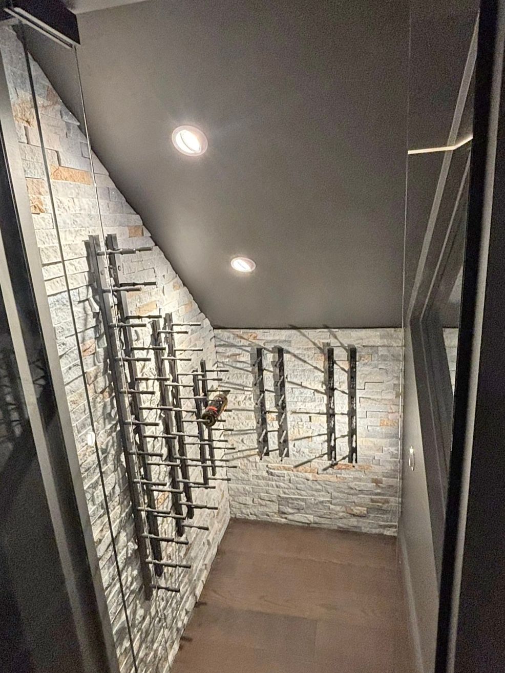 Wine cellar with stone walls, metal racks, and recessed lighting.