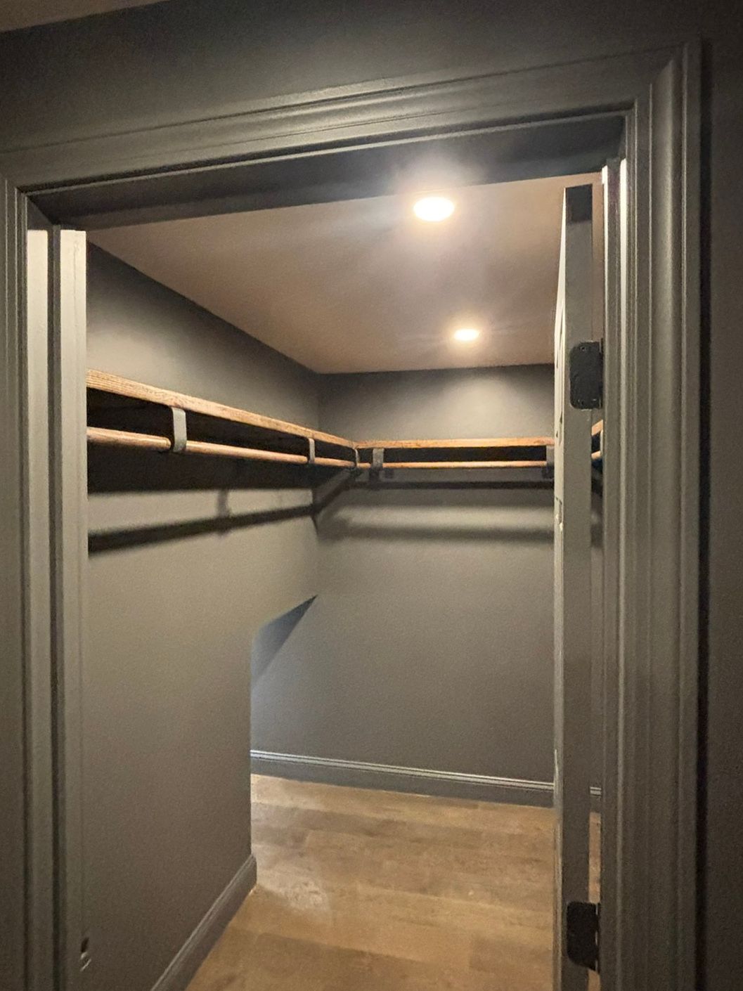 Empty walk-in closet with gray walls, wood shelves, and a light wooden floor.