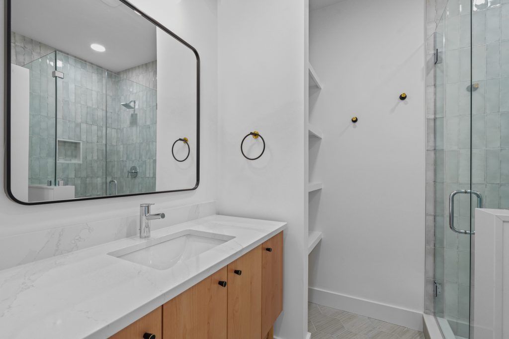 Modern bathroom with white countertops, light wood vanity, large mirror, and glass shower.
