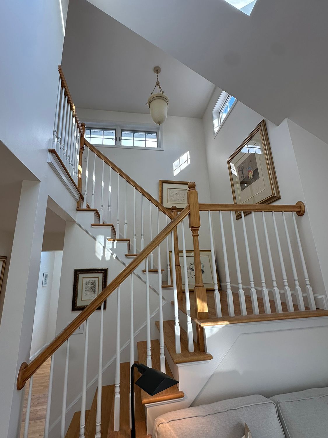 Staircase with wooden handrails, white spindles, and artwork on the walls.