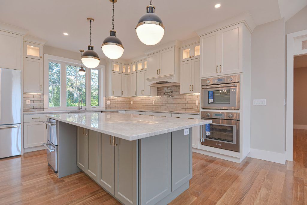 Spacious white kitchen with gray island, pendant lights, stainless steel appliances, and wood floors.
