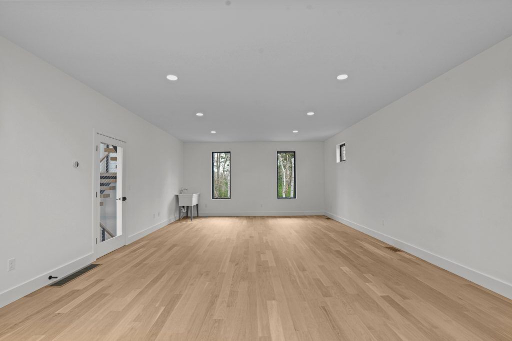 Empty room with wood floors and white walls. Two windows and recessed lighting.