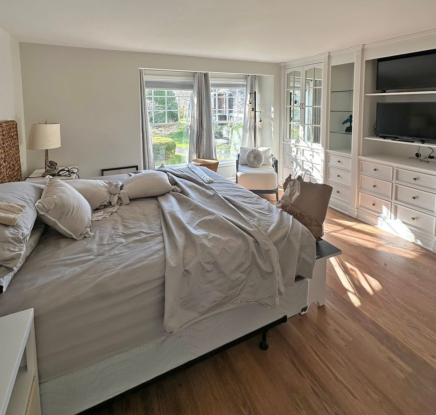 Bedroom with bed, built-in shelves, windows, hardwood floors, and natural light.