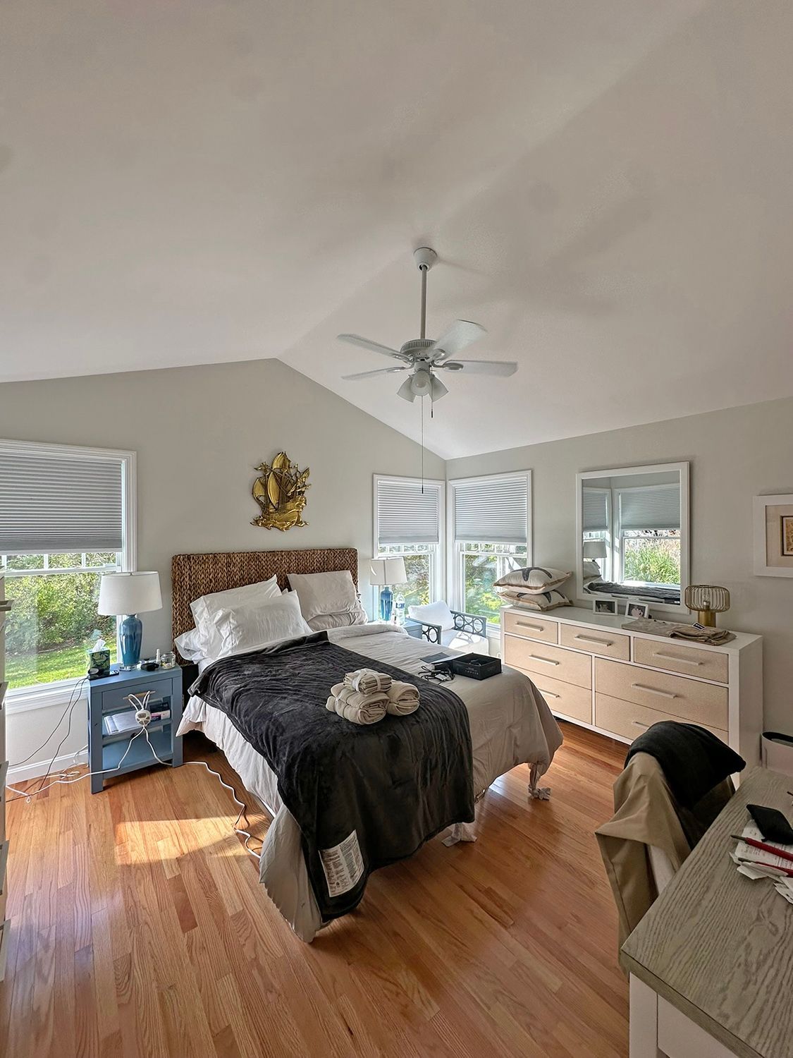 Bedroom with vaulted ceiling, hardwood floors, bed with blue accents, dresser, and windows.