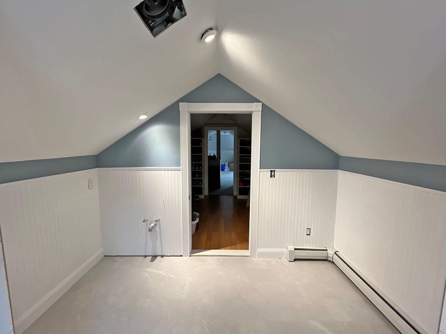 Room with white wainscoting and blue walls, doorway to another room, ceiling light.