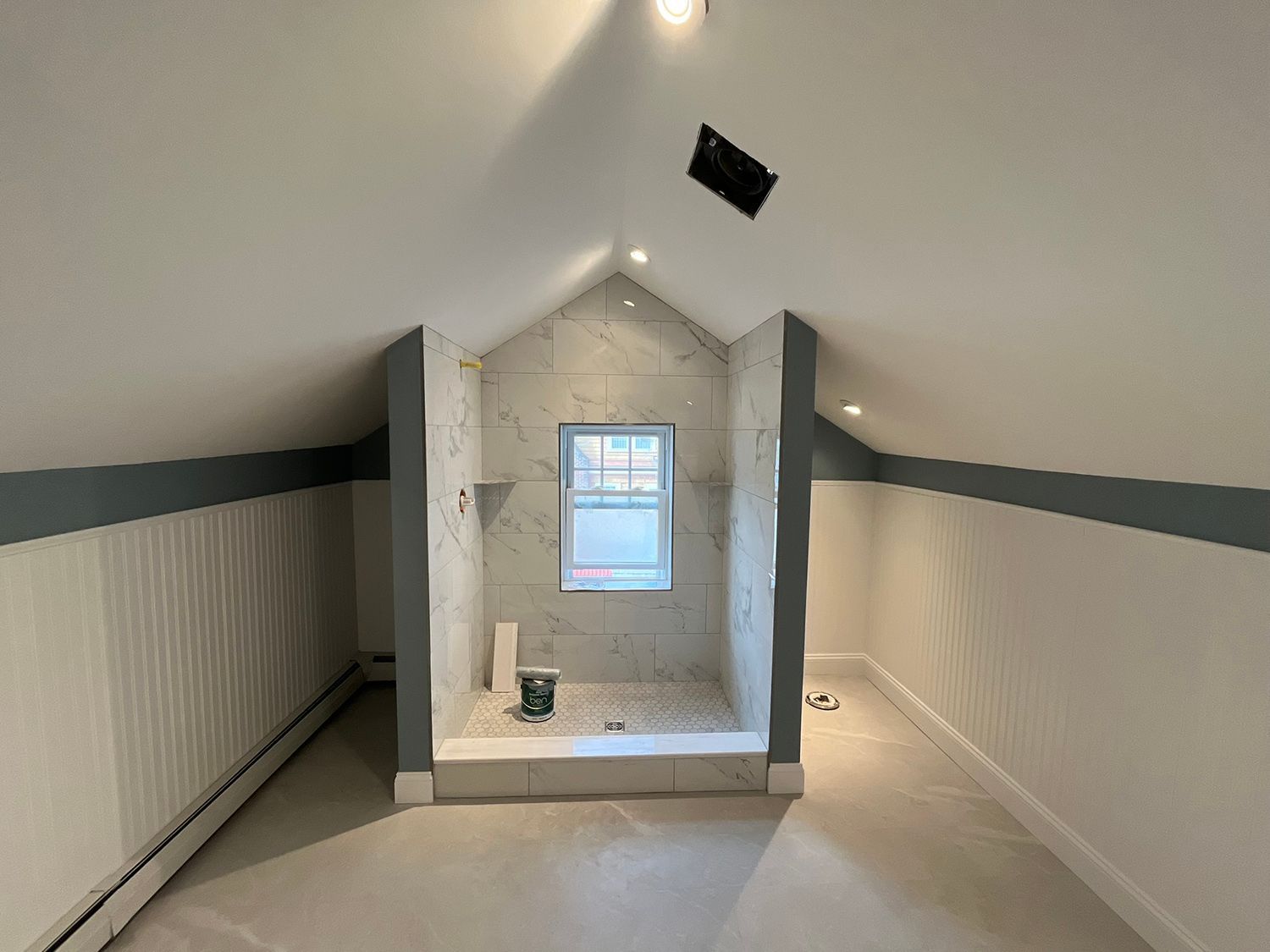 Bathroom under construction with white walls, grey shower area, and small window.