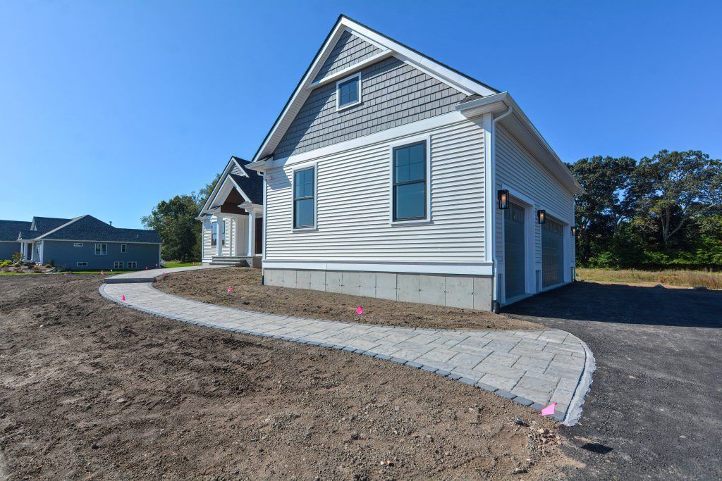New house with a paved walkway, garage, and blue sky.