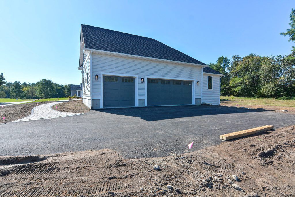 Two-car garage with gray doors on a newly paved driveway, under a clear blue sky.