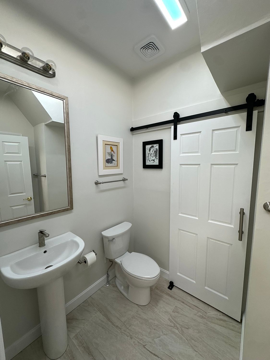 A small bathroom with a pedestal sink, toilet, and white sliding door.