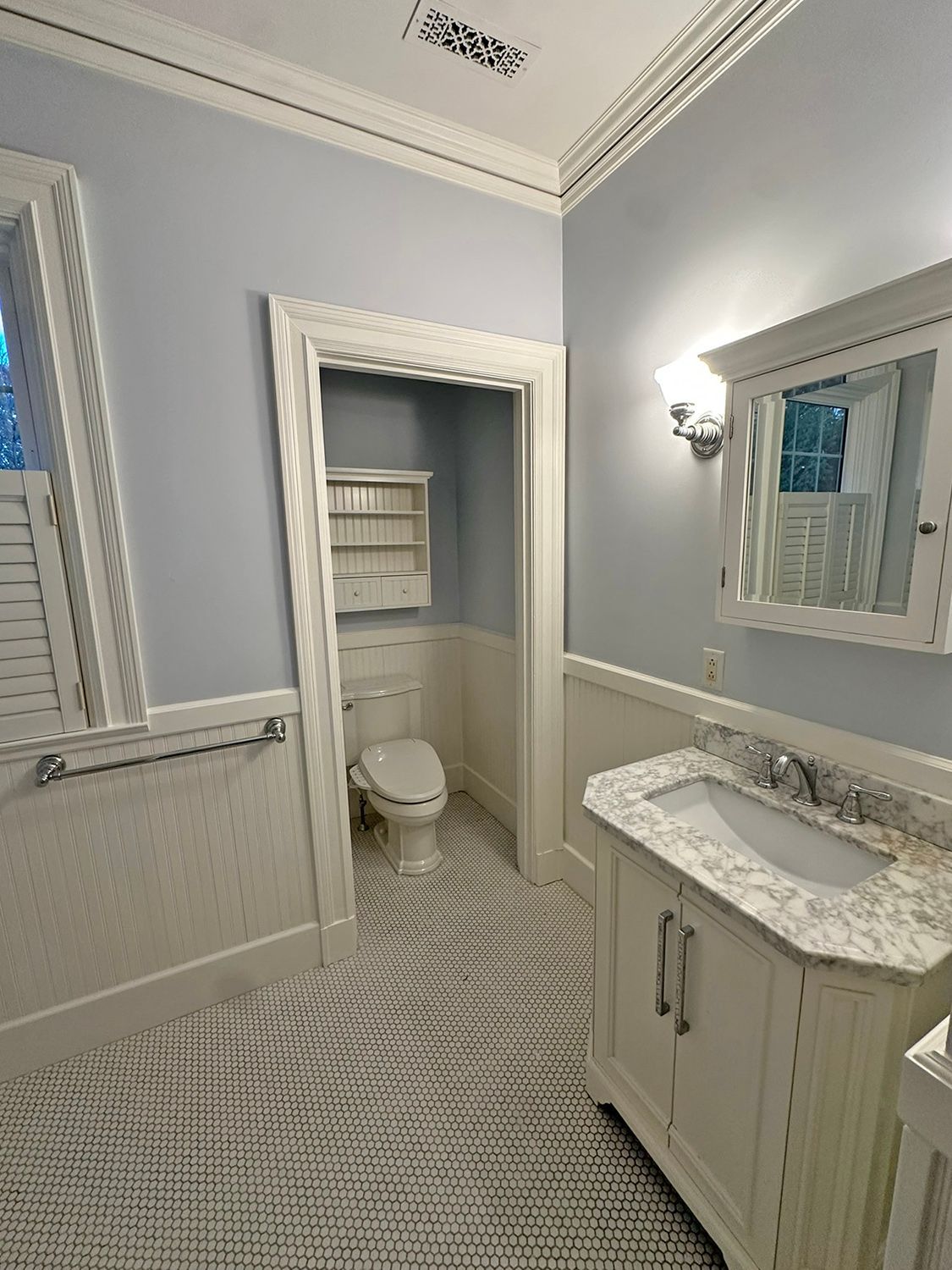 Bathroom with blue walls, white trim, vanity, toilet, and patterned floor.