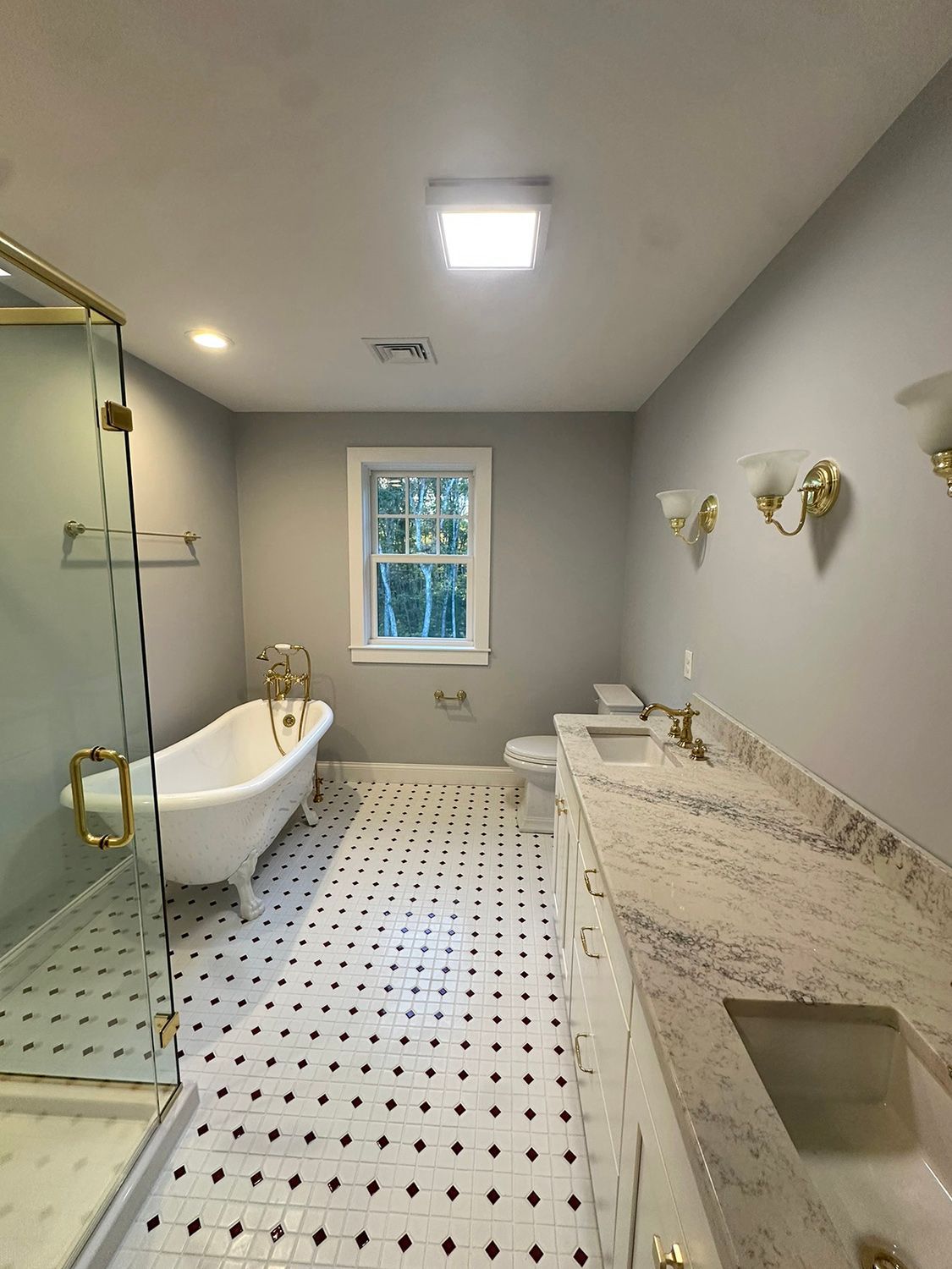 Bathroom with clawfoot tub, dual sinks with granite countertops, and black and white tiled floor.