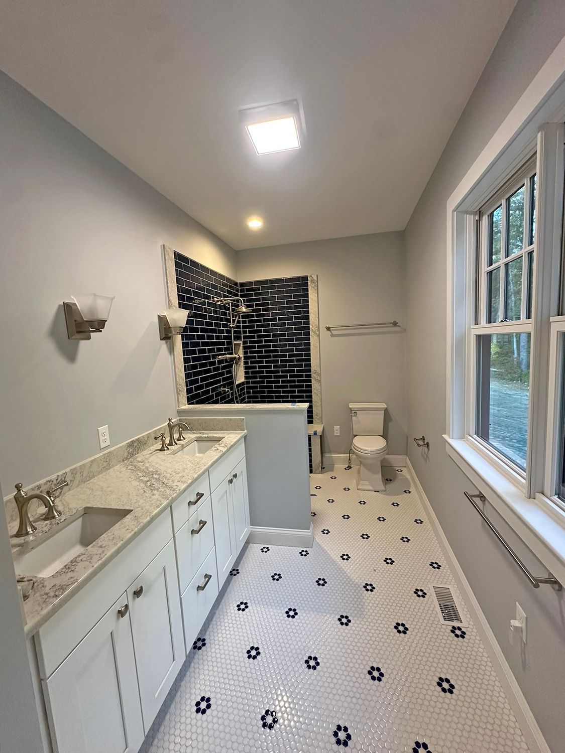 Bathroom with white cabinets, double sink, patterned floor, shower, toilet, and window.