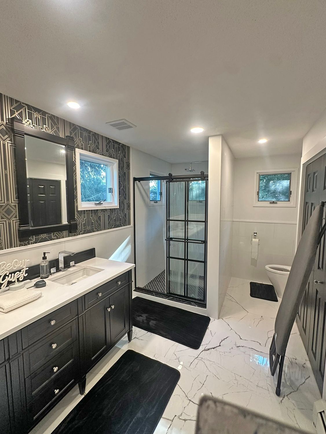 Bathroom with dark vanity, black framed shower, black and white tile.