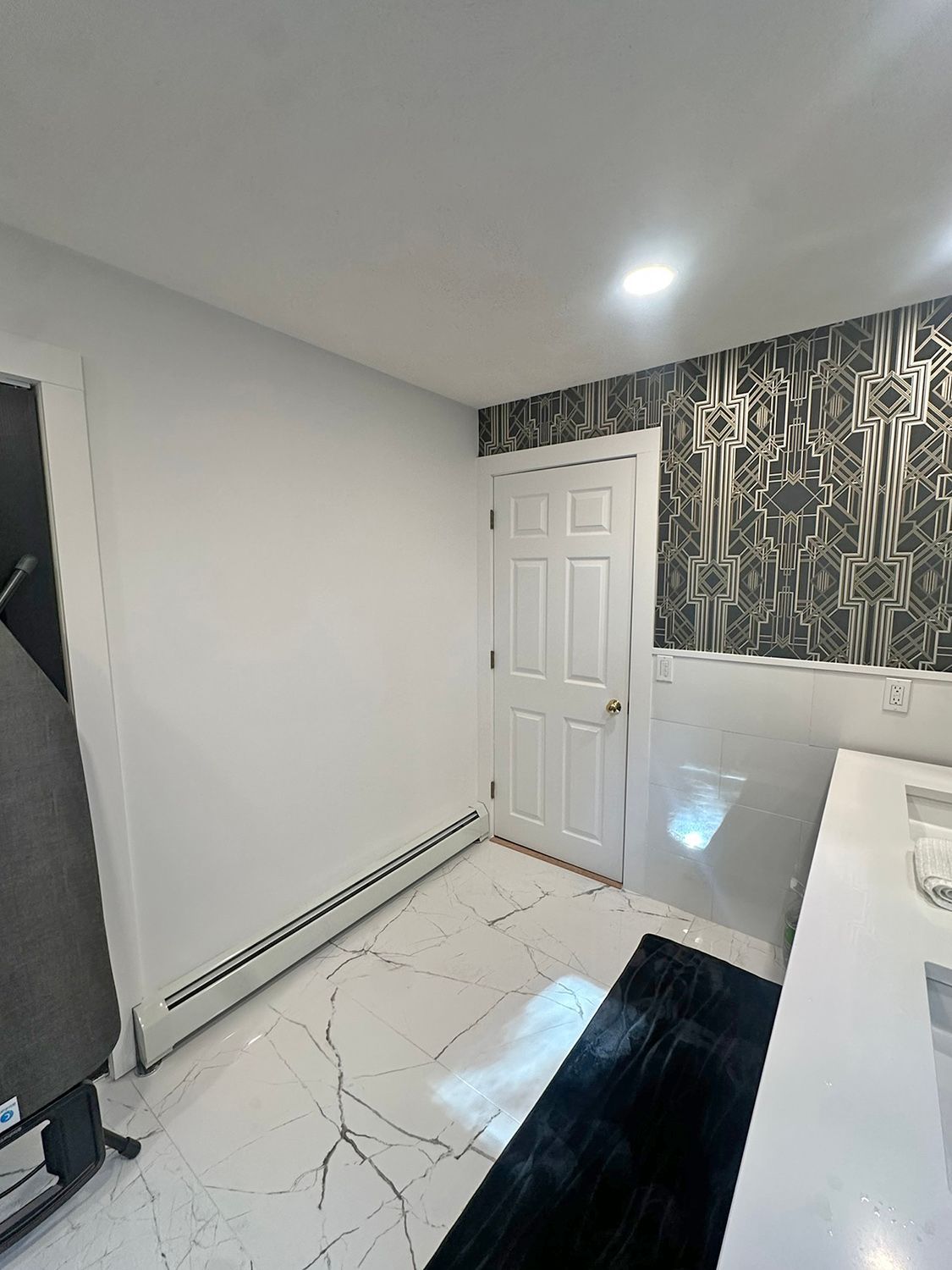 Bathroom interior with white walls, patterned accent wall, white and black floor, door, rug, and sink.