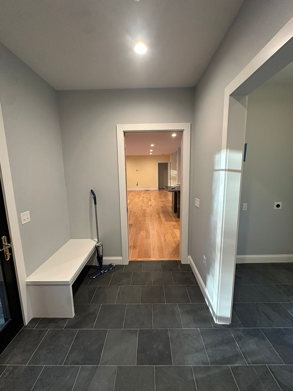 Entryway with gray walls, dark floor, bench, and door leading to a room with wood floors.