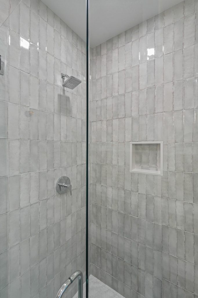 Shower with gray, textured tile walls, glass door, and chrome fixtures.