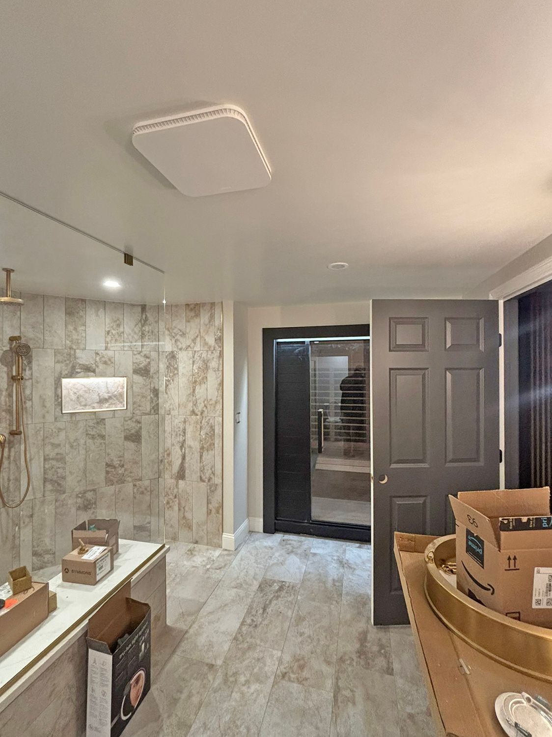 Bathroom with shower, vanity, and sauna door, boxes on floor, neutral colors.