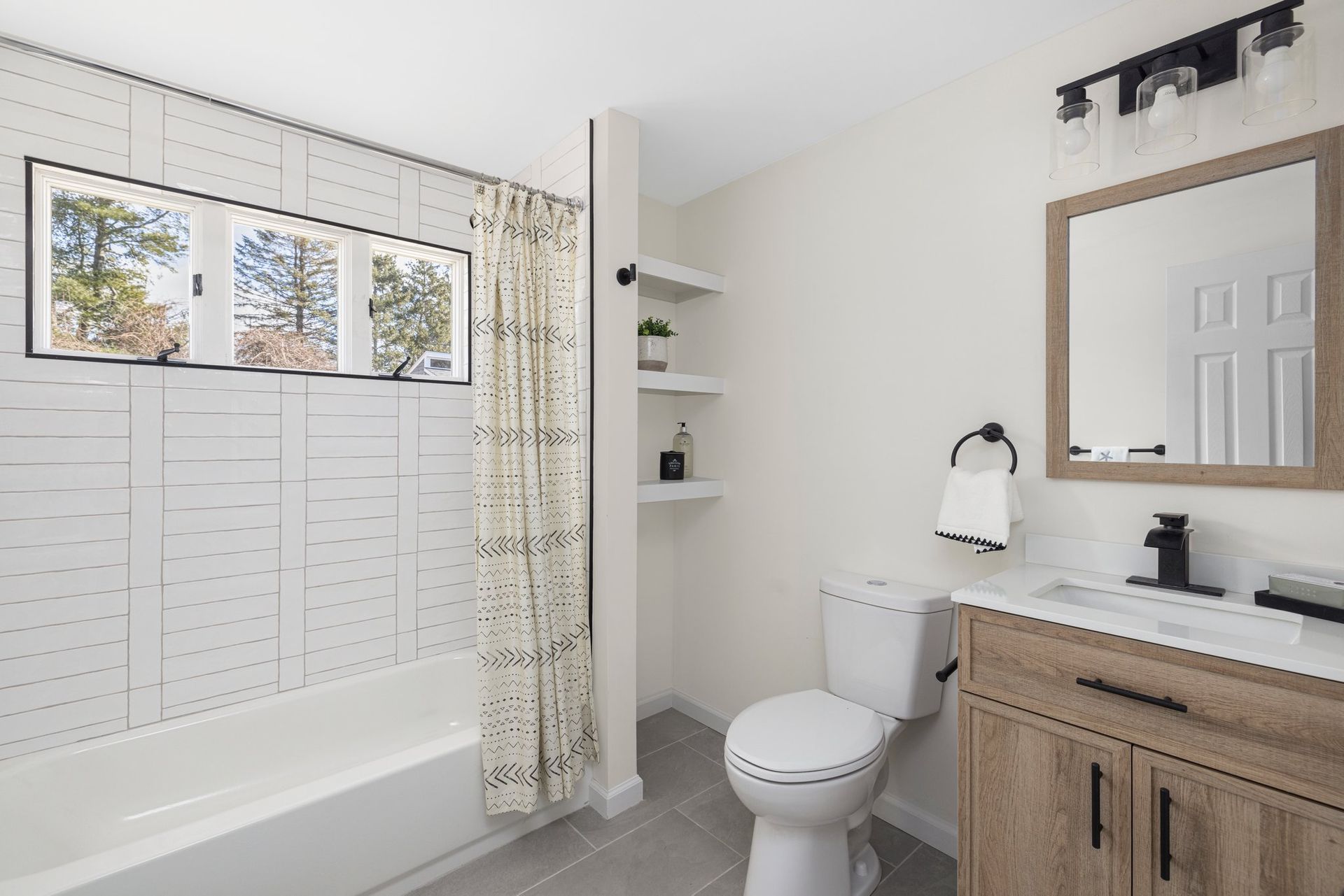 Bathroom with white tile, a bathtub, a toilet, a vanity, and floating shelves.