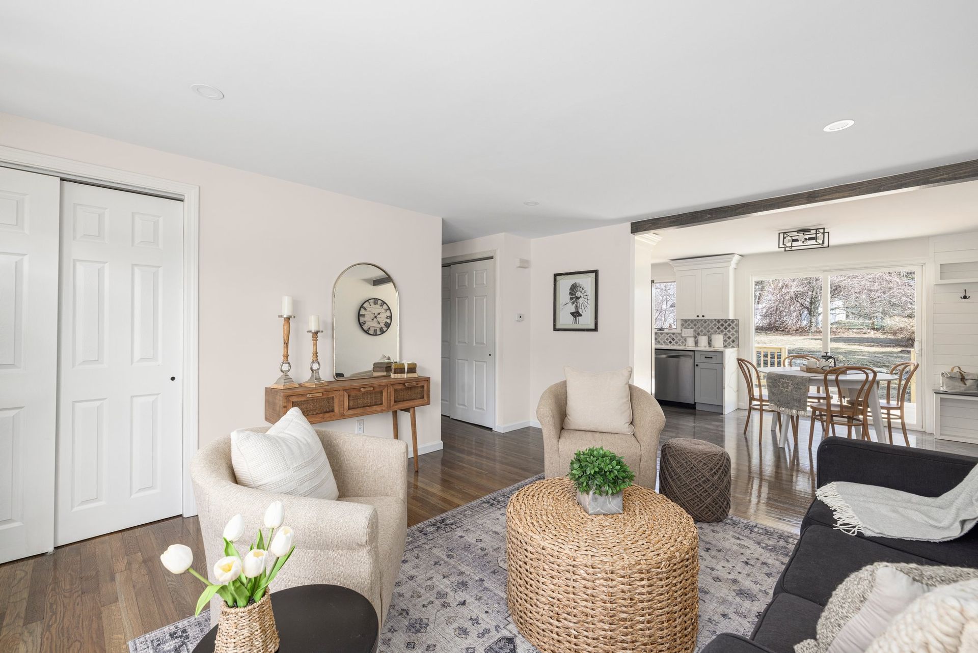 Cozy living room with seating, a woven coffee table, and open view to the kitchen and dining area.