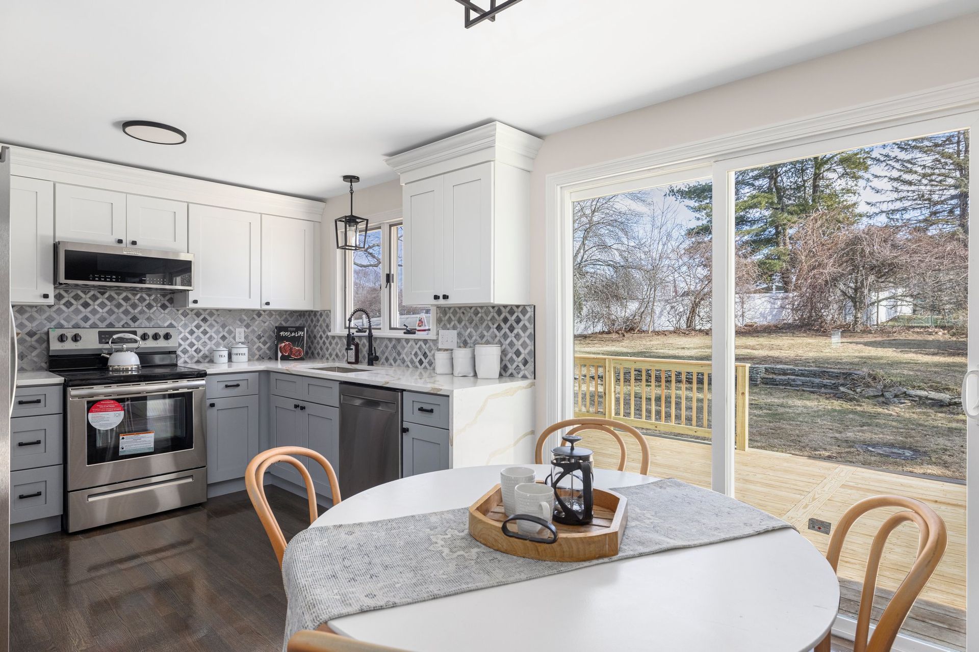 Kitchen with white and gray cabinets, stainless steel appliances, and a round dining table near sliding doors to a backyard.