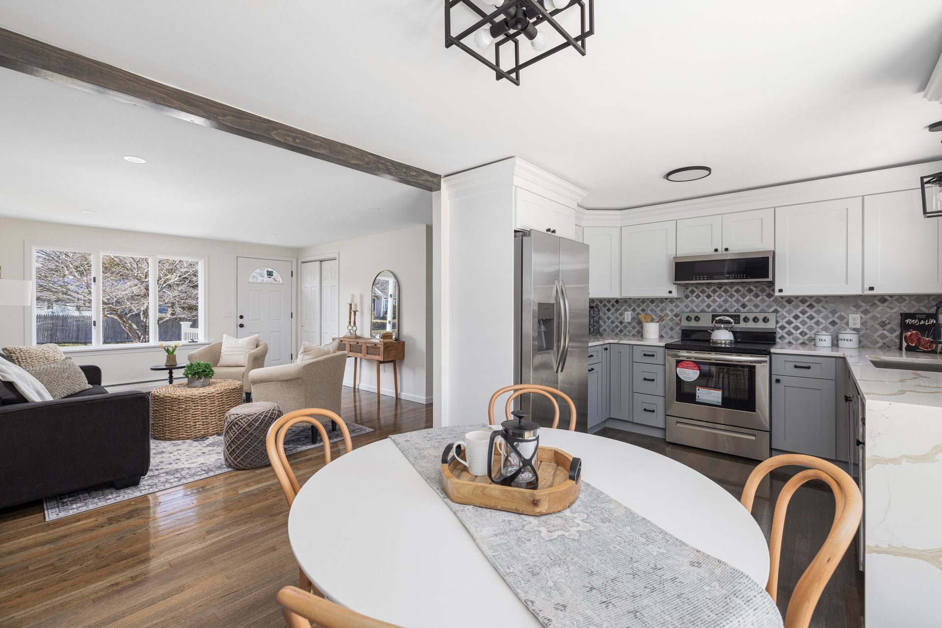Open-concept kitchen and dining area with round white table, grey cabinetry, stainless steel appliances, and wood floors.