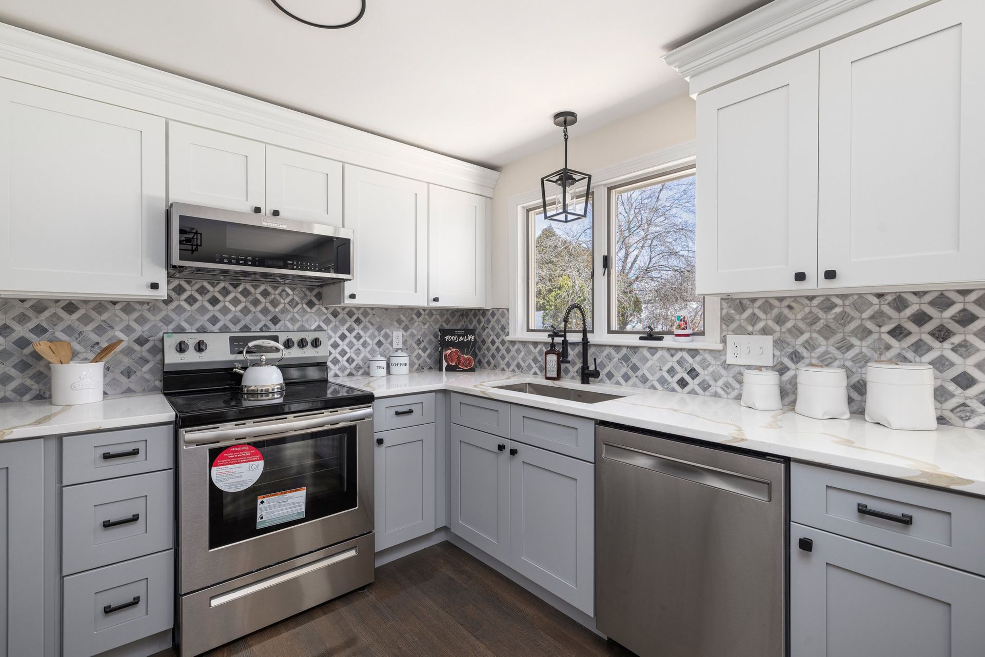 Modern kitchen with white and gray cabinets, stainless steel appliances, and patterned backsplash.