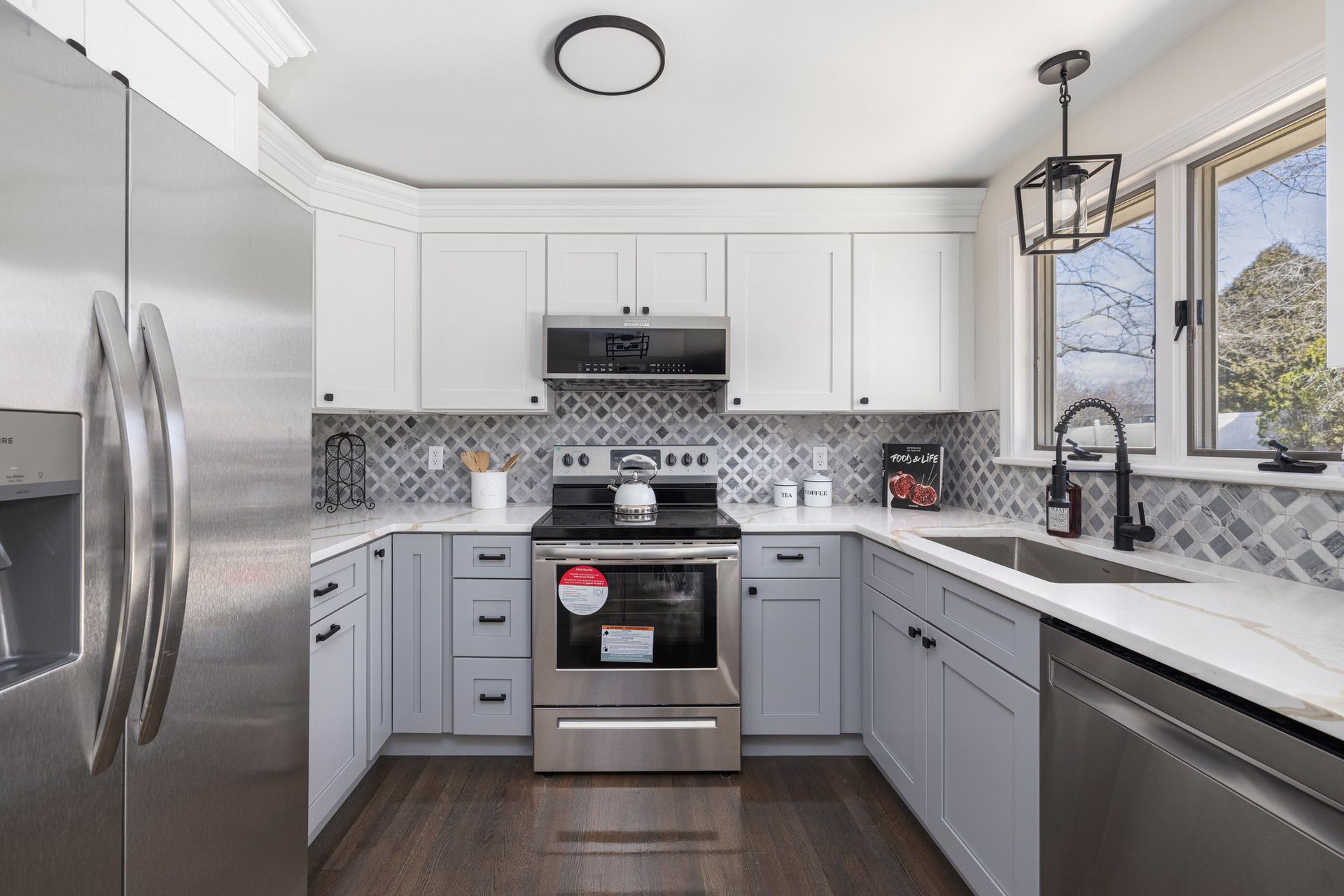 Modern kitchen with gray and white cabinets, stainless steel appliances, and a mosaic backsplash.