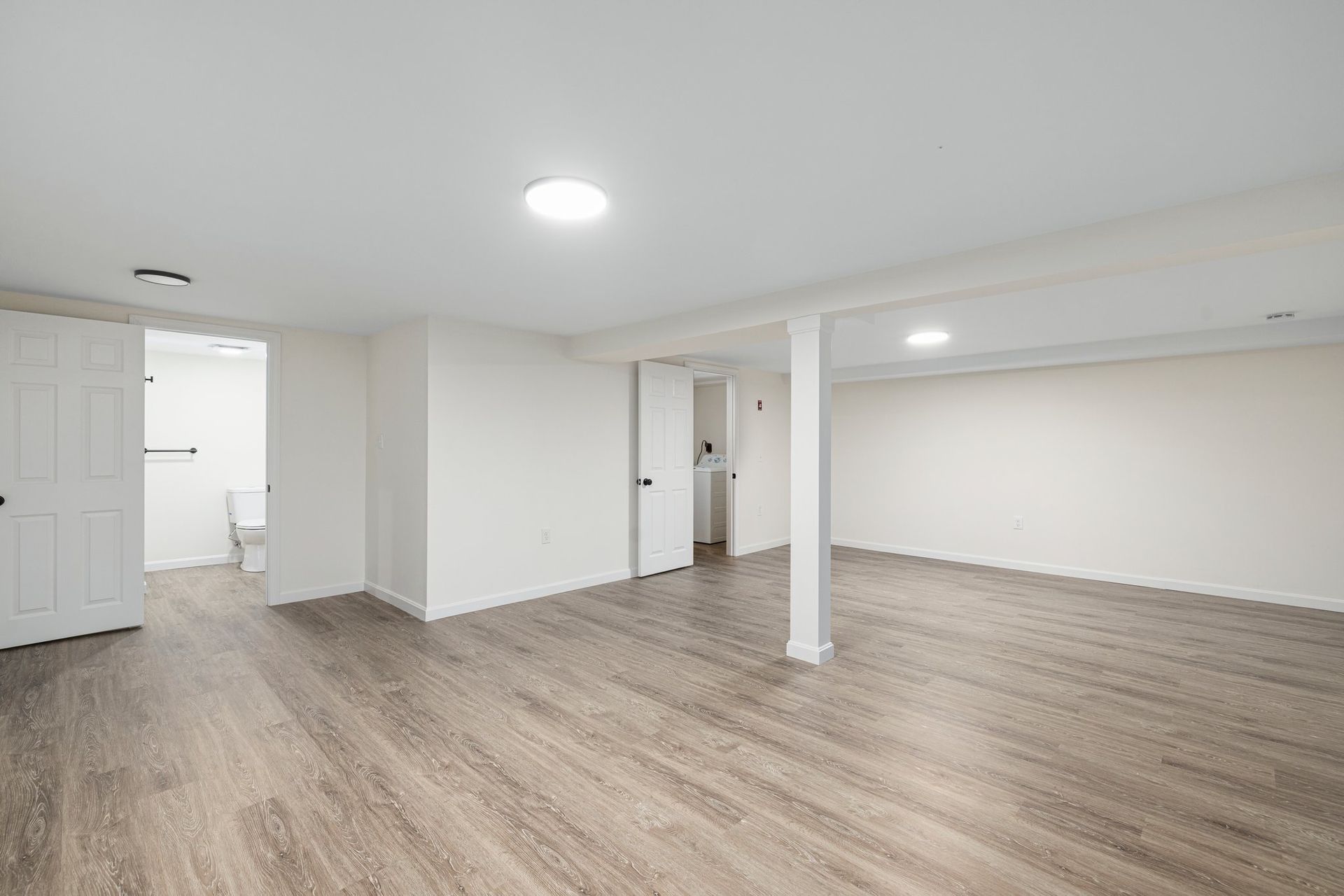 Empty, renovated room with laminate flooring, white walls, and two doorways.