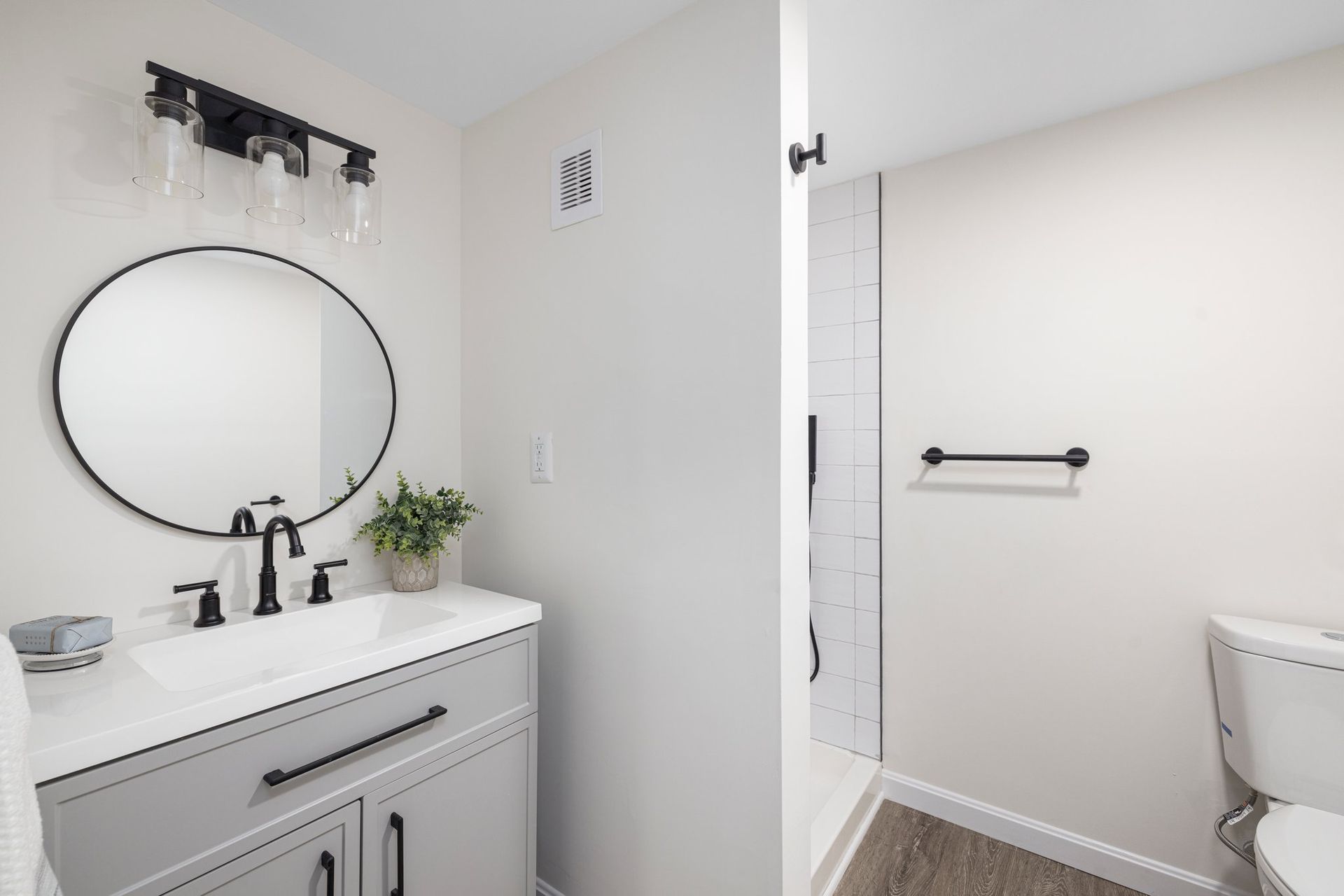 Bathroom with a round mirror, black fixtures, gray vanity, and white walls.