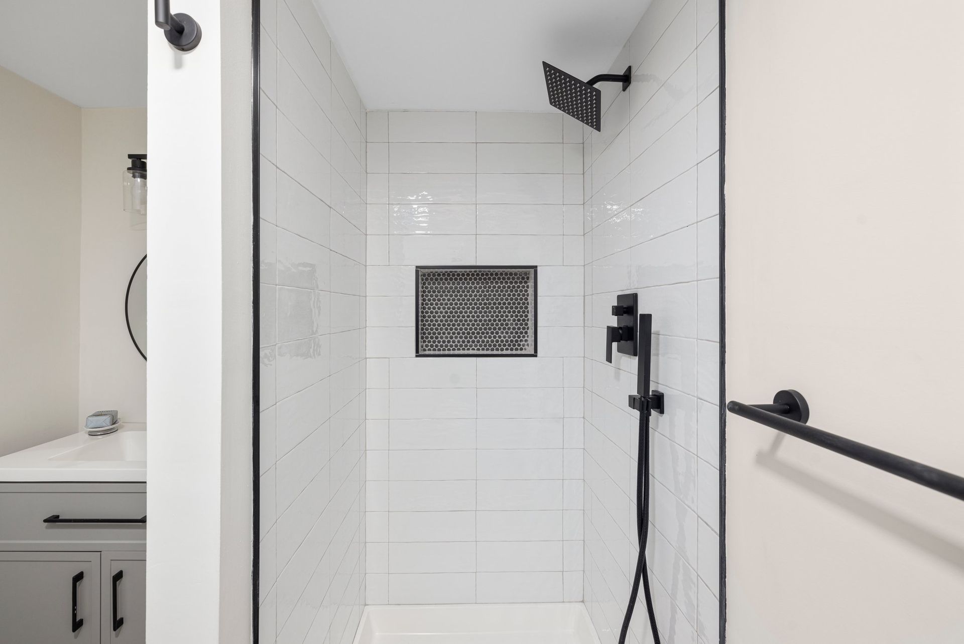 White tiled shower with black fixtures and a recessed shelf.