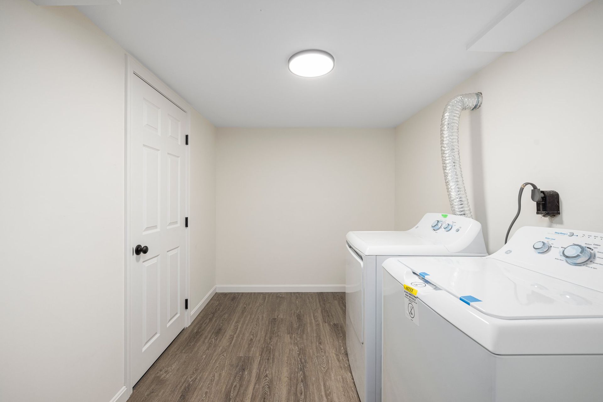 Laundry room with white appliances, closed door, and wood-look flooring.