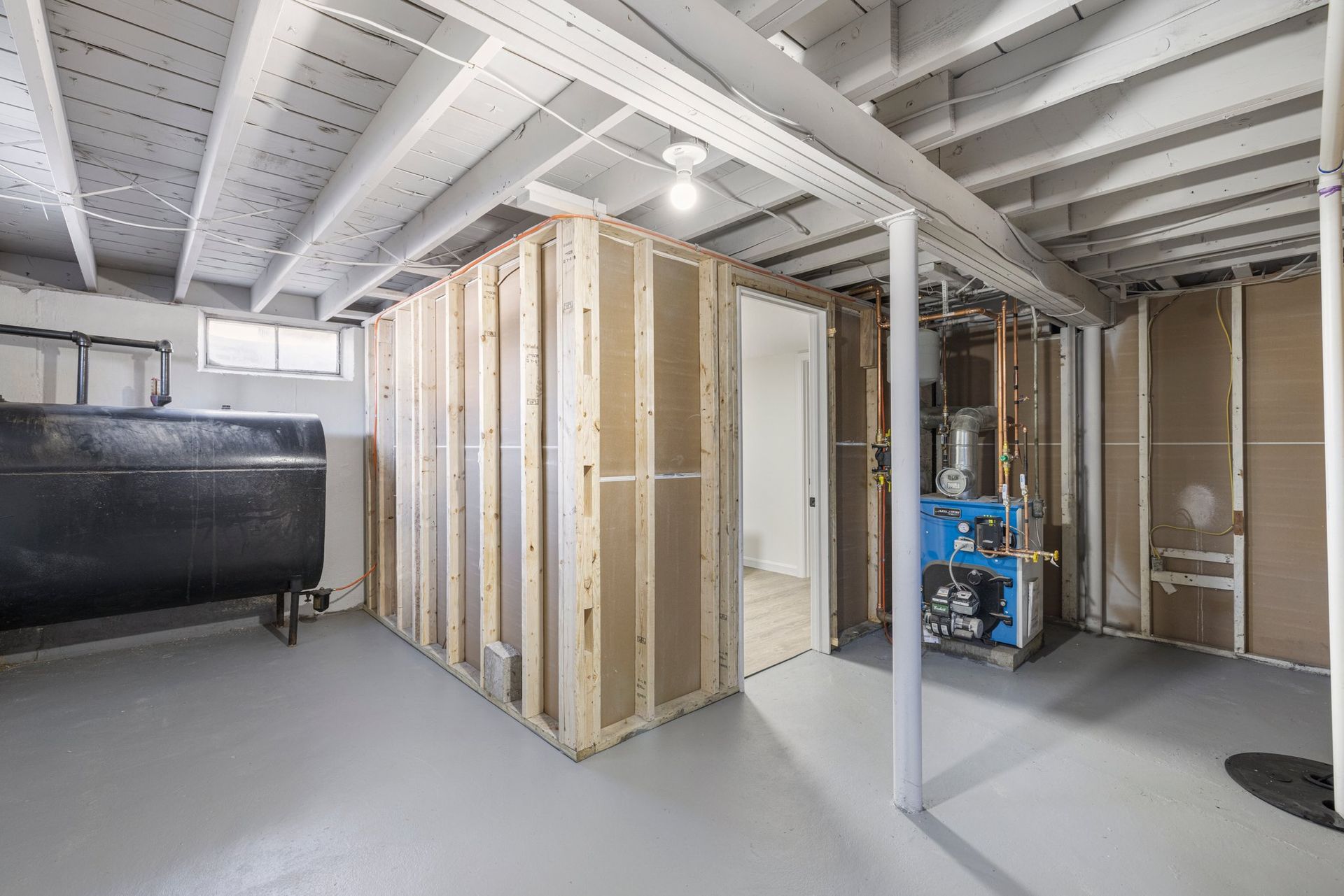 Basement with exposed framing, heating system, and oil tank; unfinished interior.