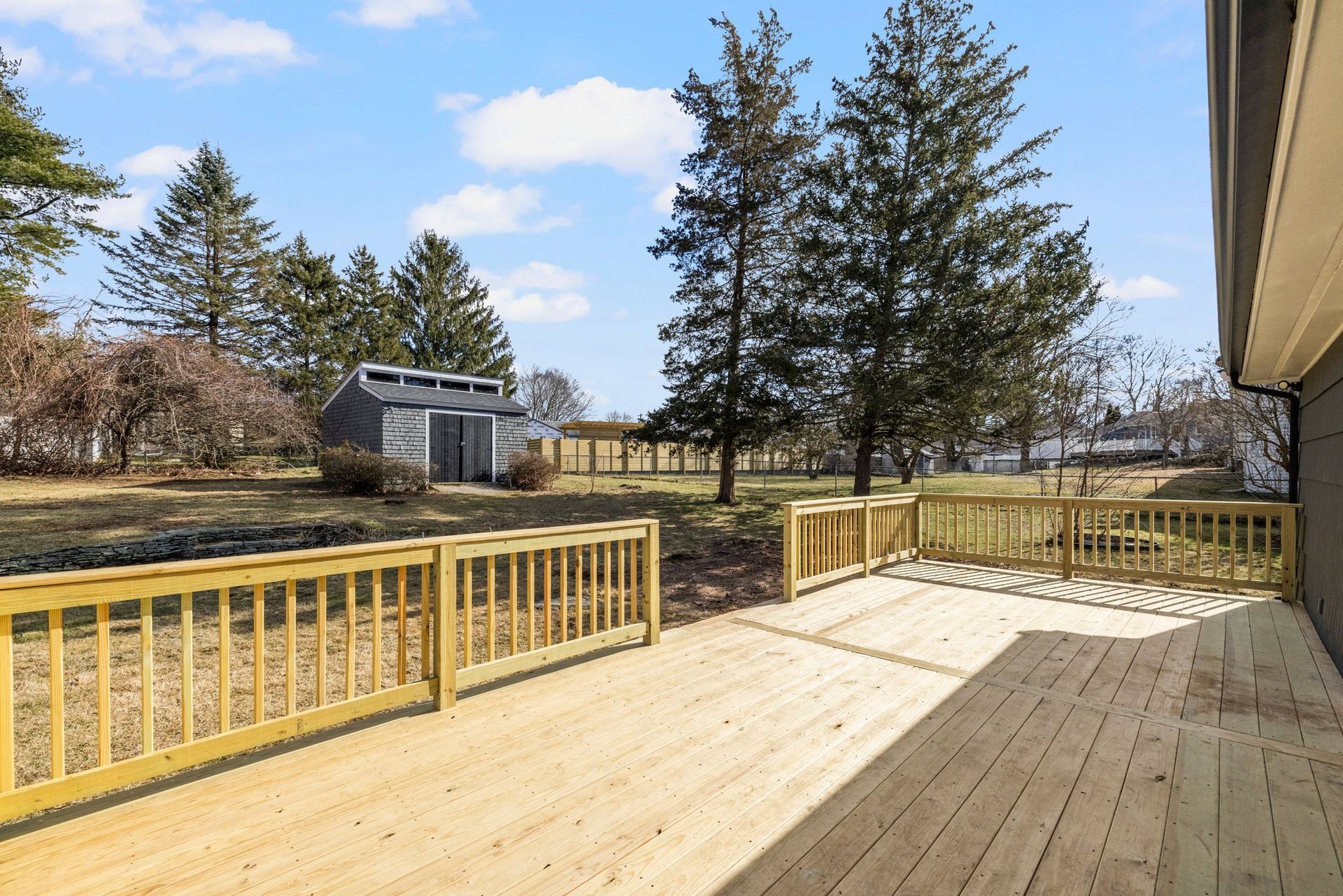 Wooden deck with railing, leading to a backyard with shed and trees.