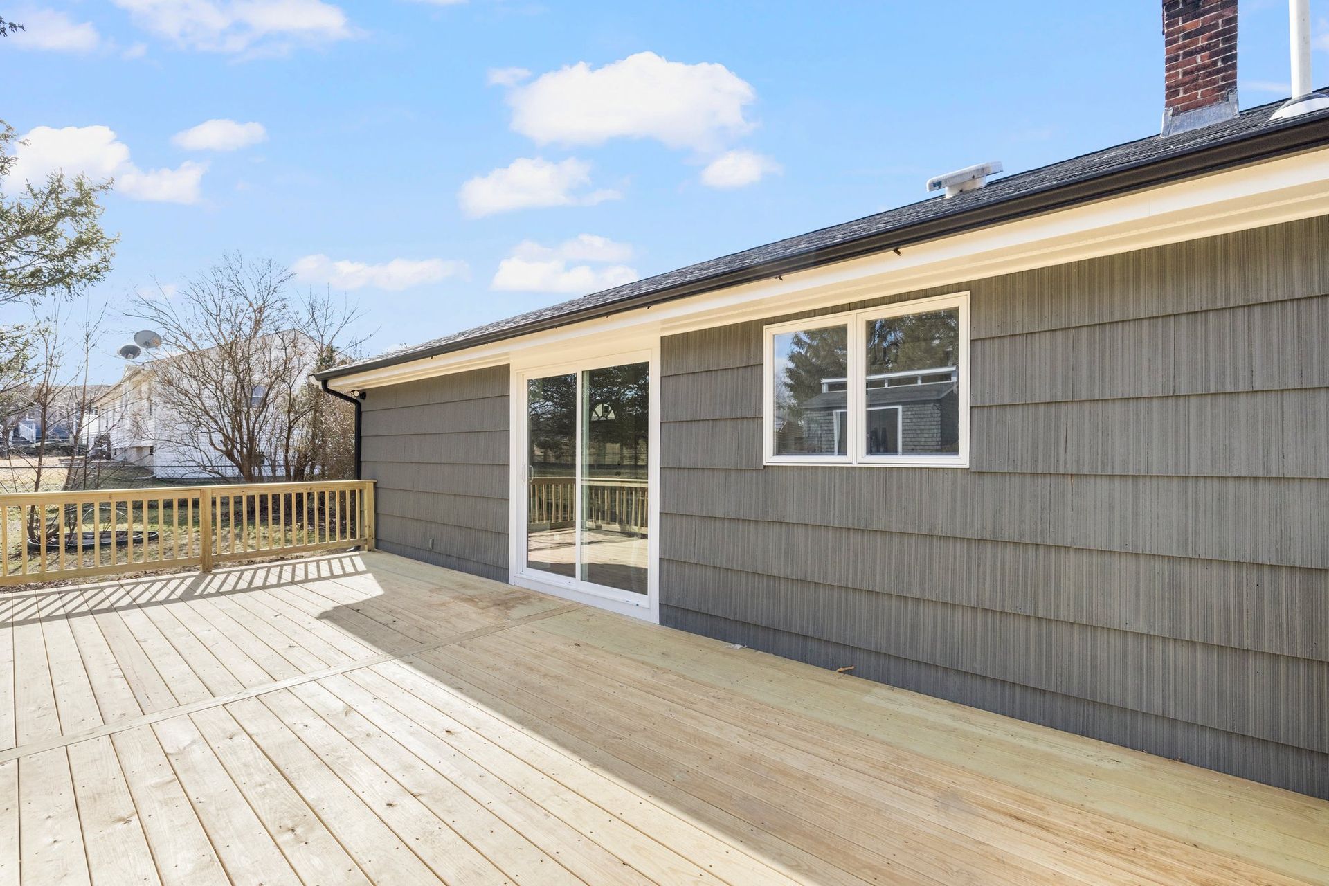 Wooden deck attached to a house with gray siding and sliding glass doors, sunny day.